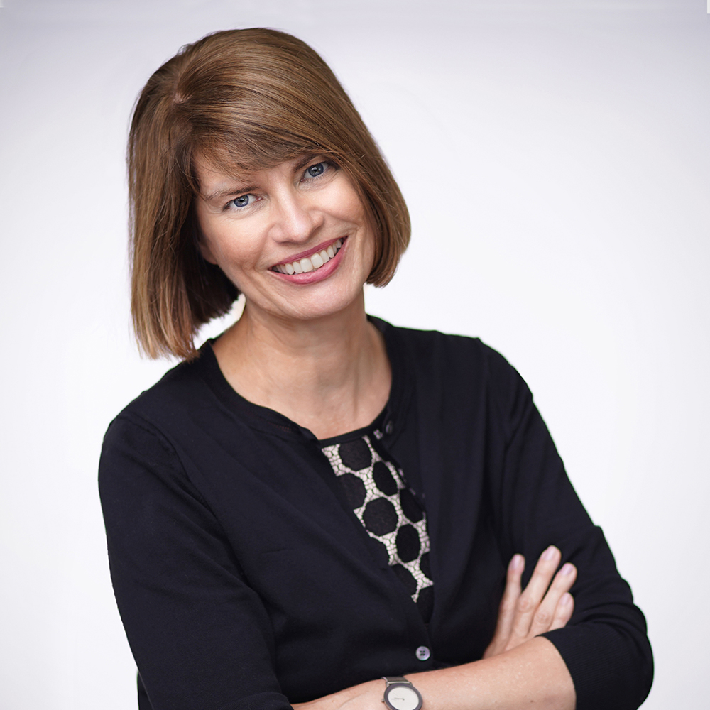 Headshot image of Christel Henke smiling. She has short, light brown hair and is wearing a black top.