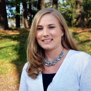 Woman in white shirt smiling in wooded area outside